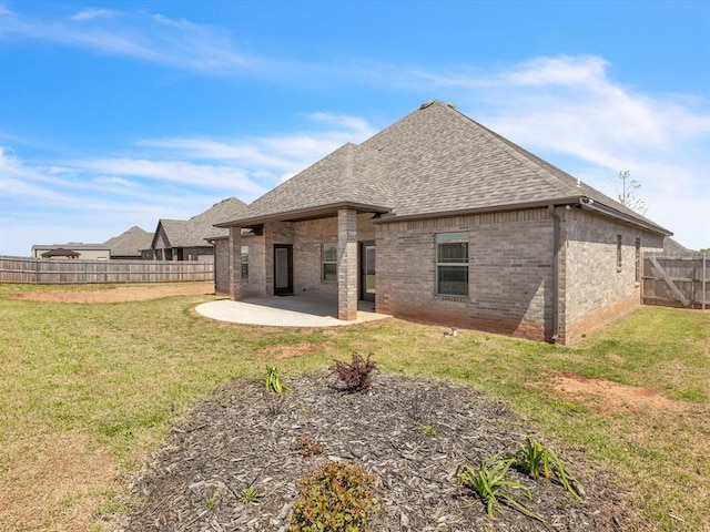 rear view of house featuring roof with shingles, brick siding, a fenced backyard, a yard, and a patio