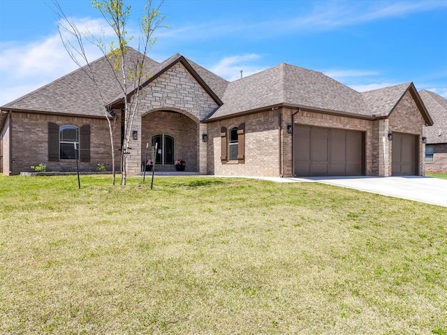 french country style house featuring a garage, a front yard, brick siding, a shingled roof, and concrete driveway