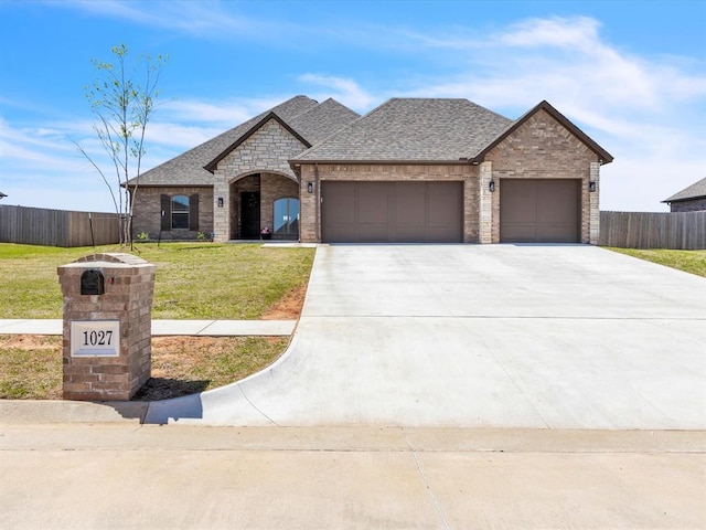 french provincial home with a garage, fence, concrete driveway, and a front yard