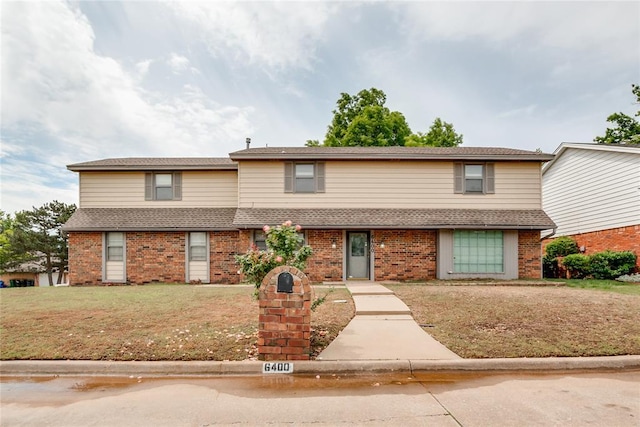 townhome / multi-family property featuring a shingled roof, a front yard, and brick siding