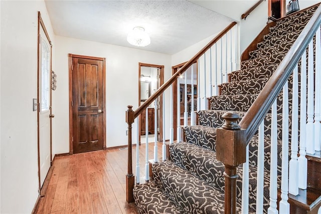 foyer entrance with wood-type flooring, a textured ceiling, baseboards, and stairs