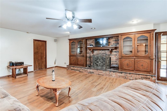 living area with a fireplace, a ceiling fan, and light wood-style flooring