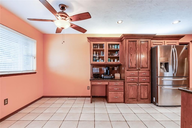 kitchen with ceiling fan, stainless steel refrigerator with ice dispenser, dark countertops, brown cabinets, and glass insert cabinets