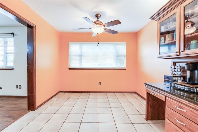 interior space with a ceiling fan, dark countertops, glass insert cabinets, and a healthy amount of sunlight