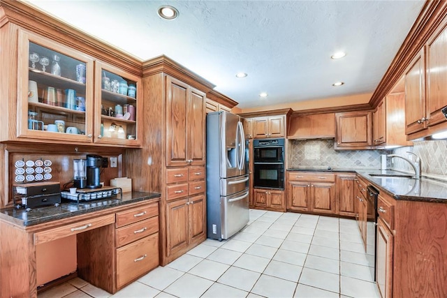 kitchen featuring brown cabinets, light tile patterned flooring, a sink, backsplash, and black appliances