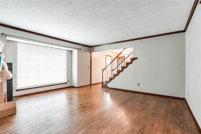 unfurnished living room with a textured ceiling, ornamental molding, baseboards, and stairway