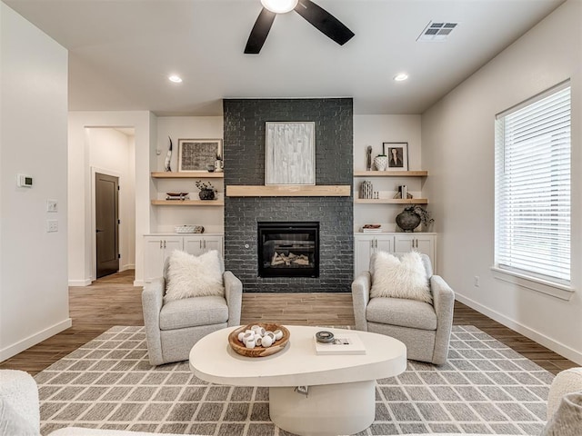 living room featuring a brick fireplace, a ceiling fan, visible vents, and wood finished floors