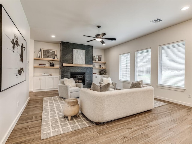 living area with a ceiling fan, visible vents, a brick fireplace, light wood-type flooring, and baseboards