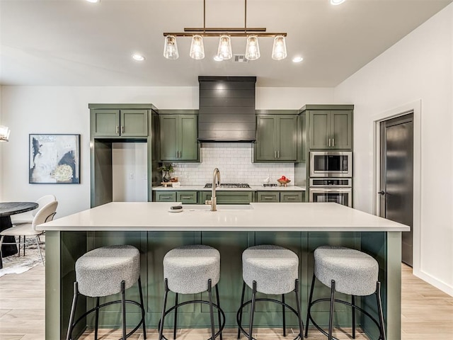 kitchen with custom exhaust hood, light wood-style floors, light countertops, appliances with stainless steel finishes, and green cabinets