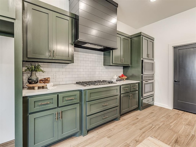 kitchen with wall chimney range hood, appliances with stainless steel finishes, green cabinetry, and light countertops