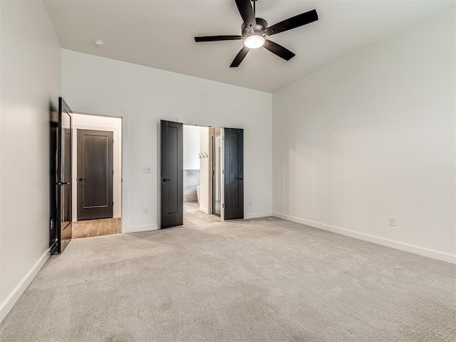 unfurnished bedroom featuring baseboards, ensuite bathroom, light carpet, and ceiling fan