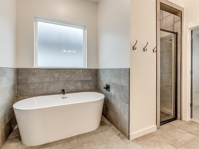 full bath featuring a freestanding bath, tile walls, tile patterned flooring, wainscoting, and a stall shower