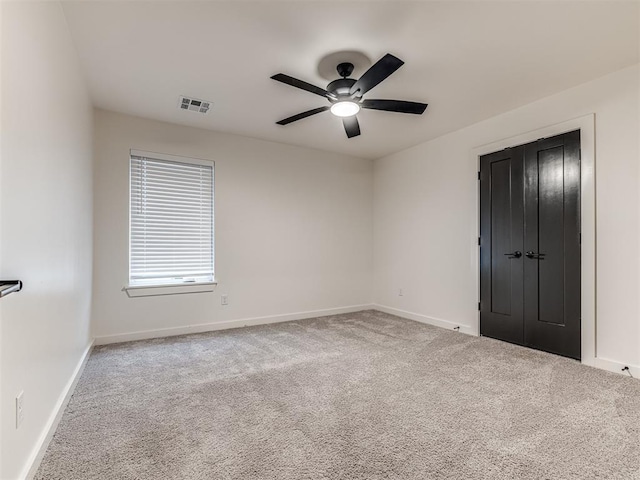 carpeted spare room with visible vents, a ceiling fan, and baseboards