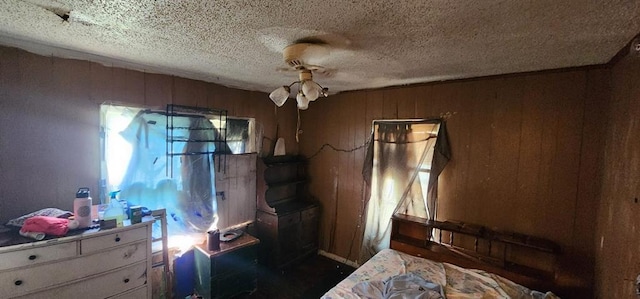 bedroom featuring wooden walls, a ceiling fan, and a textured ceiling