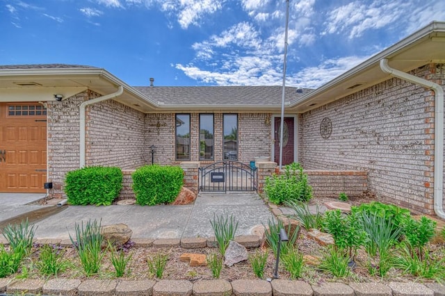 204 Sequoia Park Dr, Yukon, OK 73099 - doorway to property featuring an attached garage, a shingled roof, brick siding, and a gate