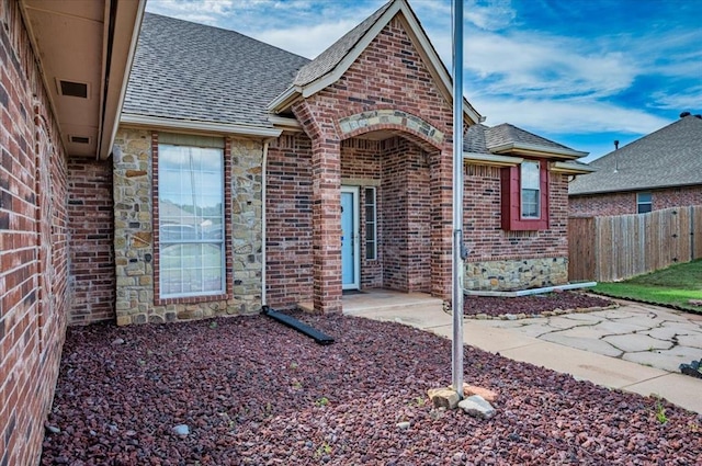exterior space with brick siding, roof with shingles, and fence