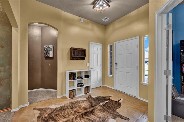 foyer with baseboards, arched walkways, tile patterned floors, and visible vents