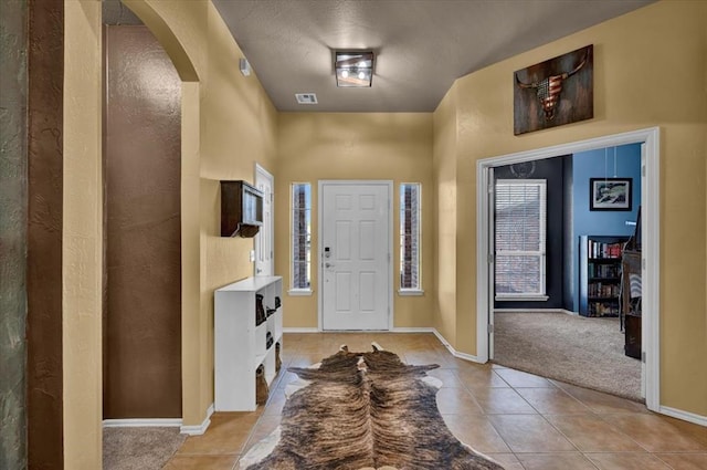 entrance foyer featuring visible vents, light tile patterned flooring, baseboards, light colored carpet, and arched walkways