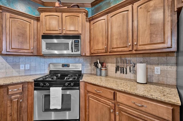 kitchen featuring appliances with stainless steel finishes, decorative backsplash, brown cabinetry, and light stone counters