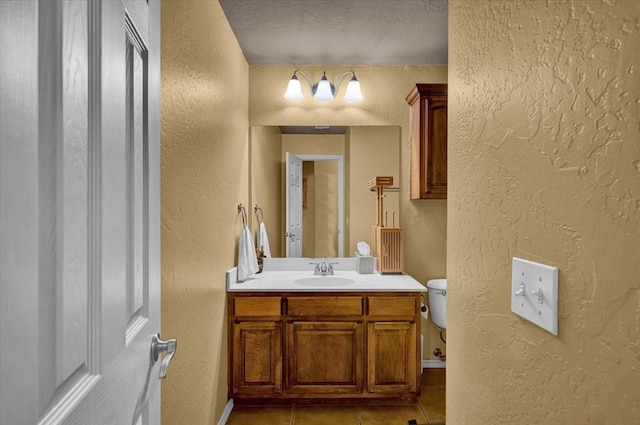 bathroom with tile patterned flooring, vanity, a textured wall, toilet, and a textured ceiling
