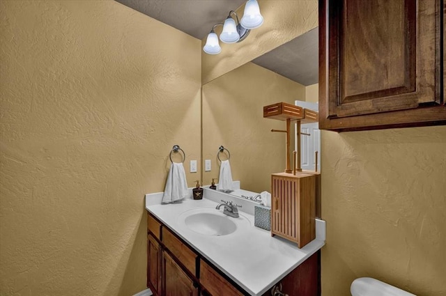 half bath with toilet, a textured wall, and vanity
