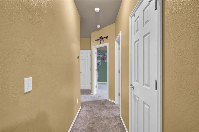 corridor featuring carpet floors, a textured wall, and baseboards
