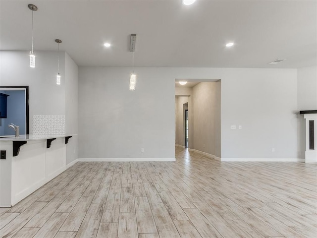 unfurnished living room featuring a sink, light wood-style flooring, recessed lighting, baseboards, and visible vents