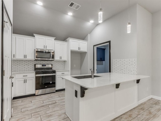 kitchen with visible vents, a peninsula, tasteful backsplash, a sink, and appliances with stainless steel finishes