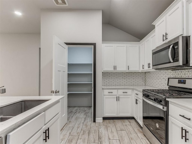 kitchen featuring decorative backsplash, appliances with stainless steel finishes, vaulted ceiling, a sink, and white cabinetry