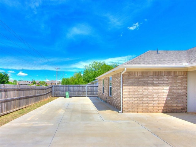 view of side of home with brick siding, a fenced backyard, a patio area, and roof with shingles