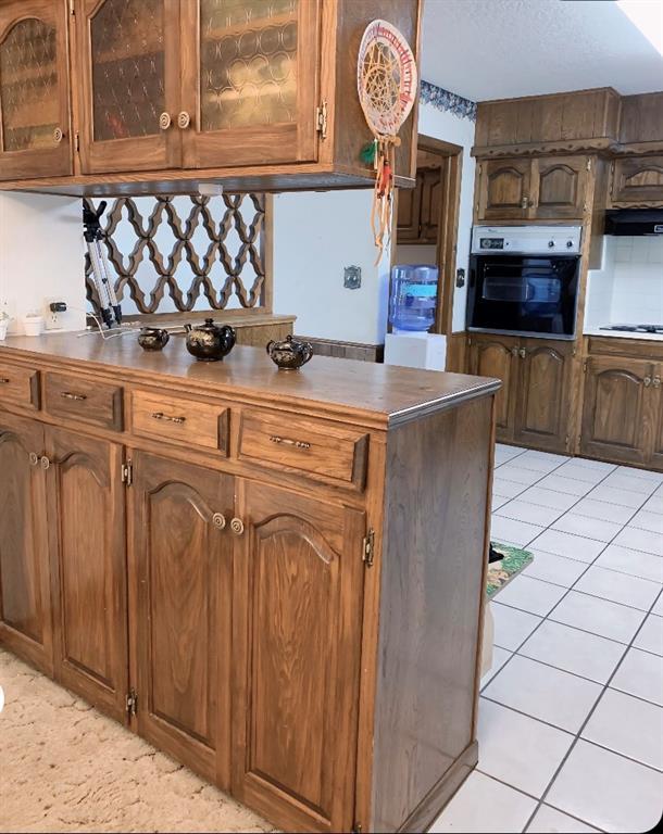 310 Walter Way, Anadarko, OK 73005 - kitchen featuring light tile patterned floors, glass insert cabinets, brown cabinets, black oven, and dark countertops