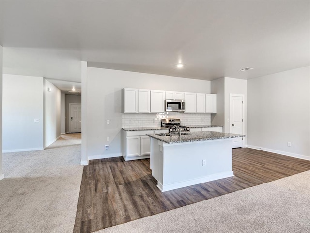 kitchen with stainless steel appliances, dark stone countertops, a center island with sink, and dark colored carpet
