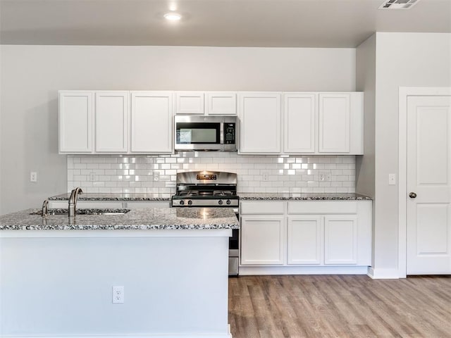 kitchen featuring appliances with stainless steel finishes, a sink, light wood-style flooring, decorative backsplash, and stone counters