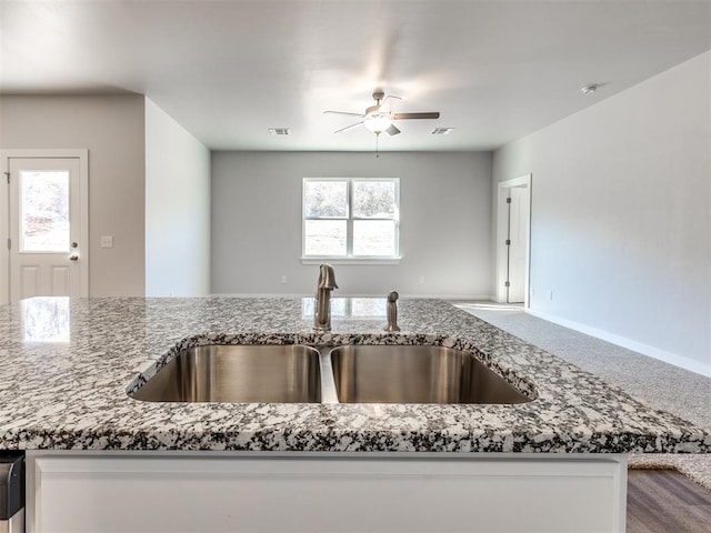 kitchen with carpet floors, open floor plan, ceiling fan, a sink, and stone counters