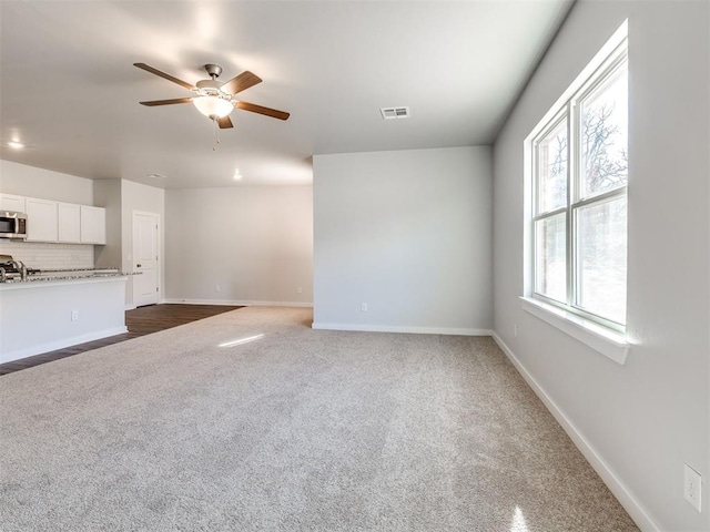 unfurnished living room featuring a ceiling fan, baseboards, visible vents, and dark carpet