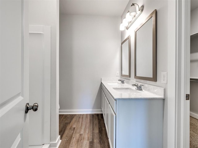 full bathroom featuring double vanity, a sink, baseboards, and wood finished floors