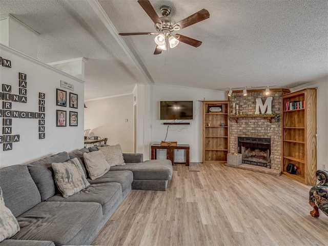 living room with crown molding, ceiling fan, a fireplace, a textured ceiling, and light wood-type flooring