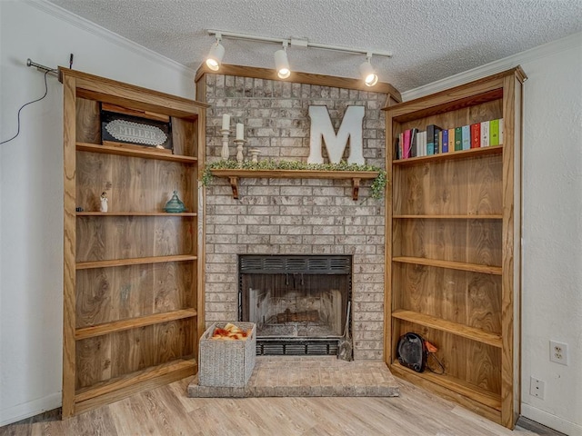 unfurnished living room with a textured ceiling, ornamental molding, a brick fireplace, and wood finished floors