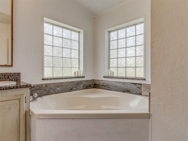 full bath featuring a textured wall, a garden tub, and vanity