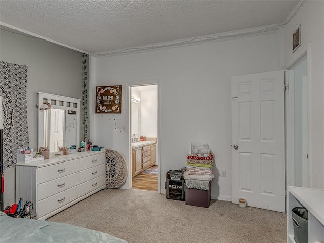 bedroom with a textured ceiling, light colored carpet, ensuite bathroom, and visible vents