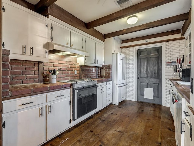 kitchen with brick wall, range with gas stovetop, freestanding refrigerator, under cabinet range hood, and visible vents