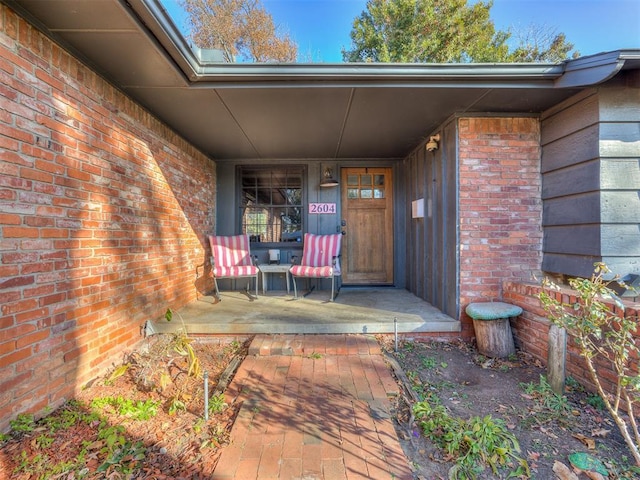 view of exterior entry with a porch and brick siding