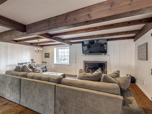 living area featuring a brick fireplace, a notable chandelier, beam ceiling, and dark wood-style floors