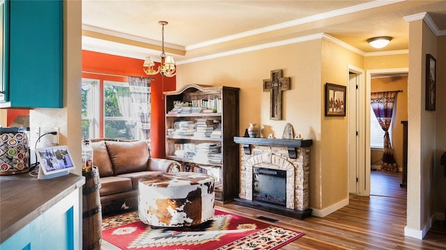 living area featuring crown molding, an inviting chandelier, a stone fireplace, baseboards, and wood finished floors