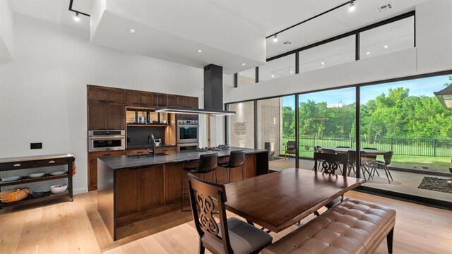 dining room with light wood-type flooring, a towering ceiling, and track lighting