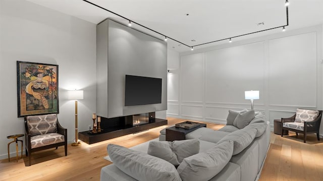 living room featuring rail lighting, light wood finished floors, and a decorative wall