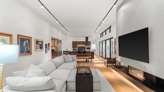 living room featuring rail lighting, light wood-type flooring, and a towering ceiling