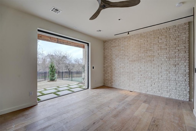 unfurnished room with brick wall, wood-type flooring, a smoke detector, ceiling fan, and baseboards