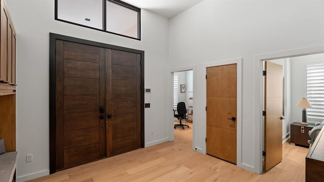 entrance foyer with light wood finished floors, baseboards, and a towering ceiling