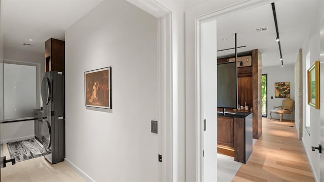 hallway with stacked washer / dryer, track lighting, baseboards, and light wood-style floors